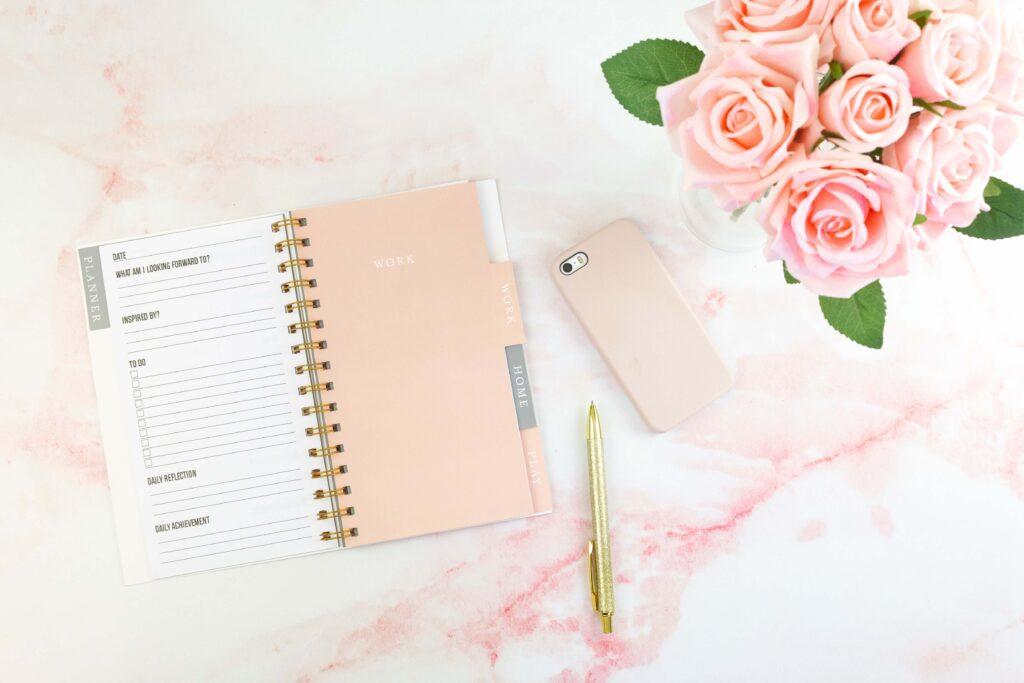 flat lay photo of pink journal laying open on a table with a pink phone and gold pen